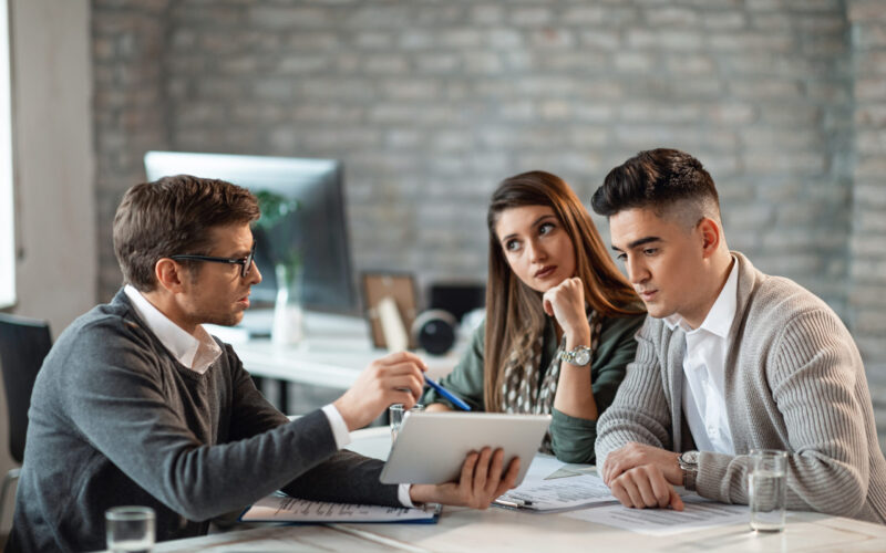 Financial advisor and young couple using touchpad on a meeting.